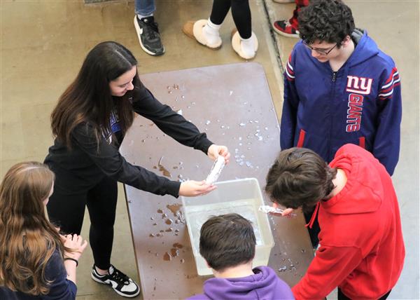  students at a table with a container of water trying to see how many candy hearts will float